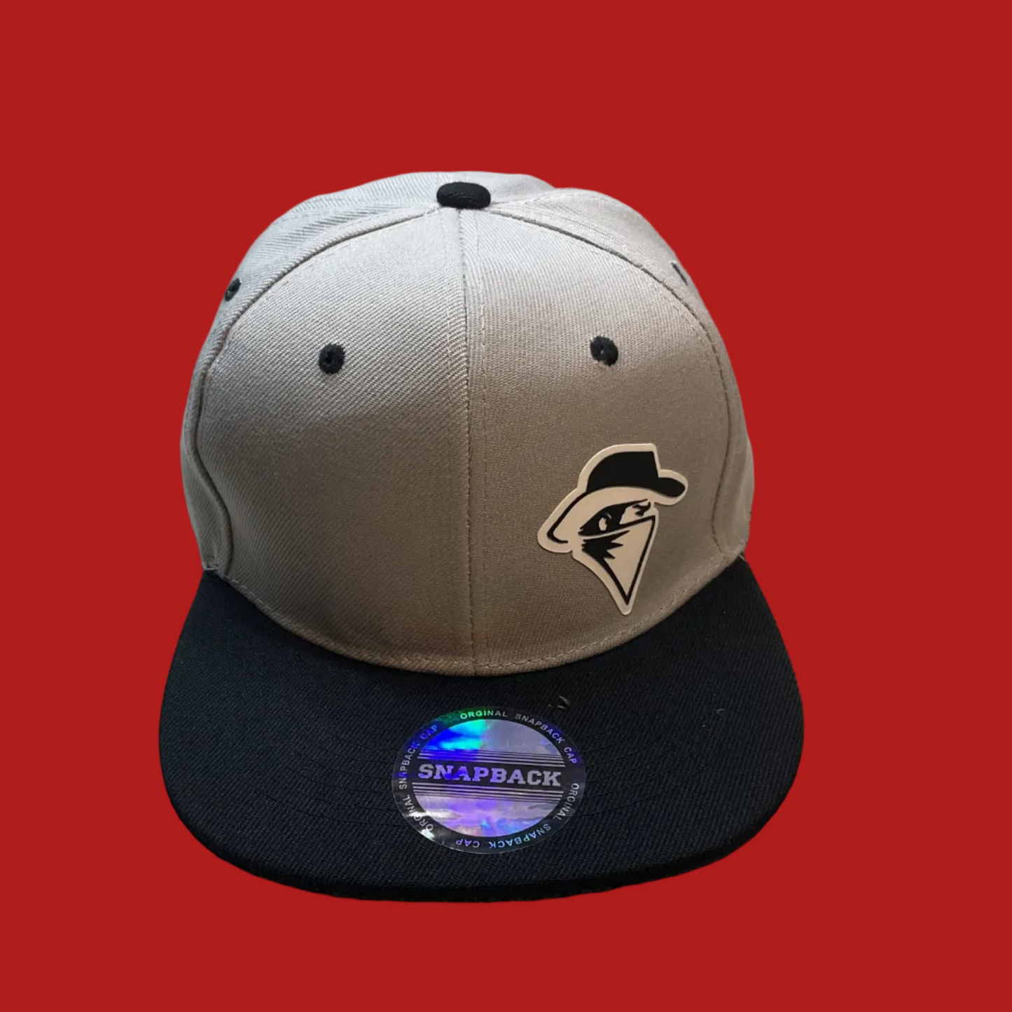A gray and black Snapback cap with a black visor and a black, white, and gray embroidered logo on the front, resting on a textured beige fabric surface.